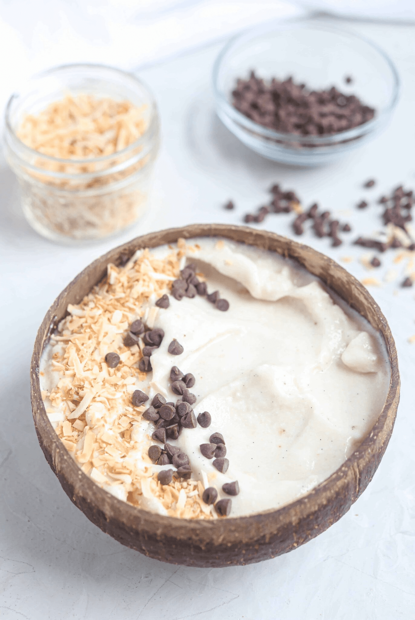 coconut vanilla smoothie bowl topped with toasted coconut and mini chocolate chips in a natural coconut shell.