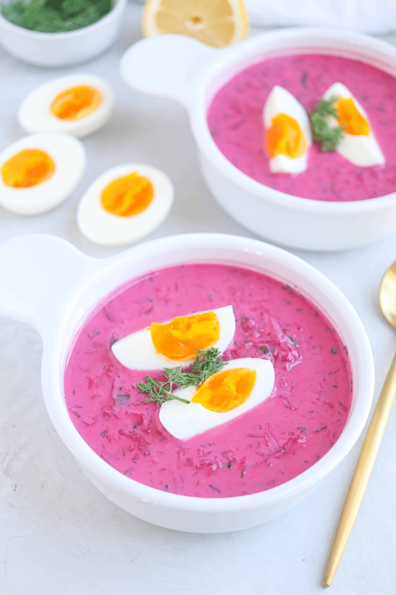 Polish cold beet soup in a white bowl with 2 quarters of boiled ehh on top.
