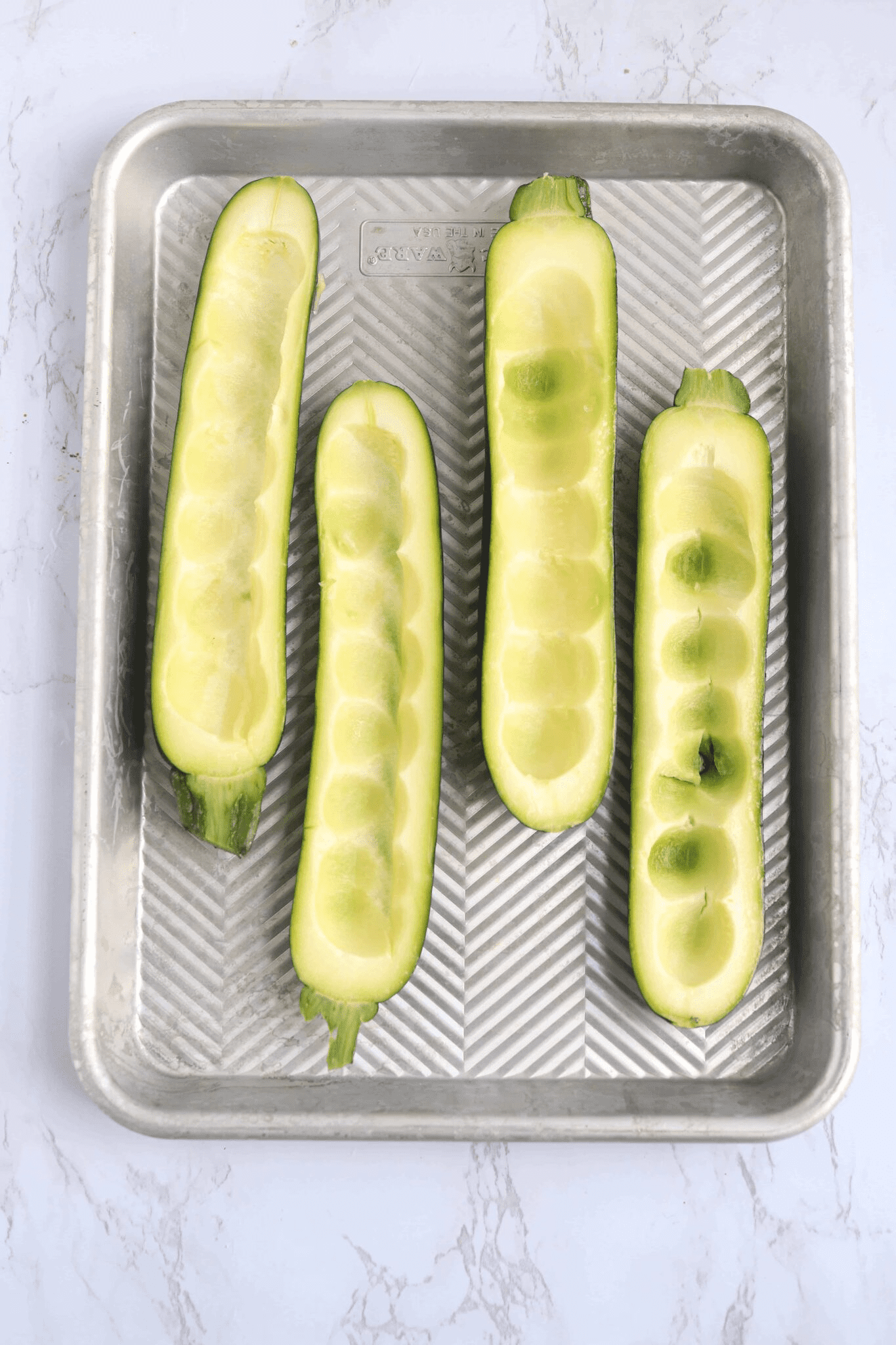 four scooped out zucchini halves on a baking tray. 