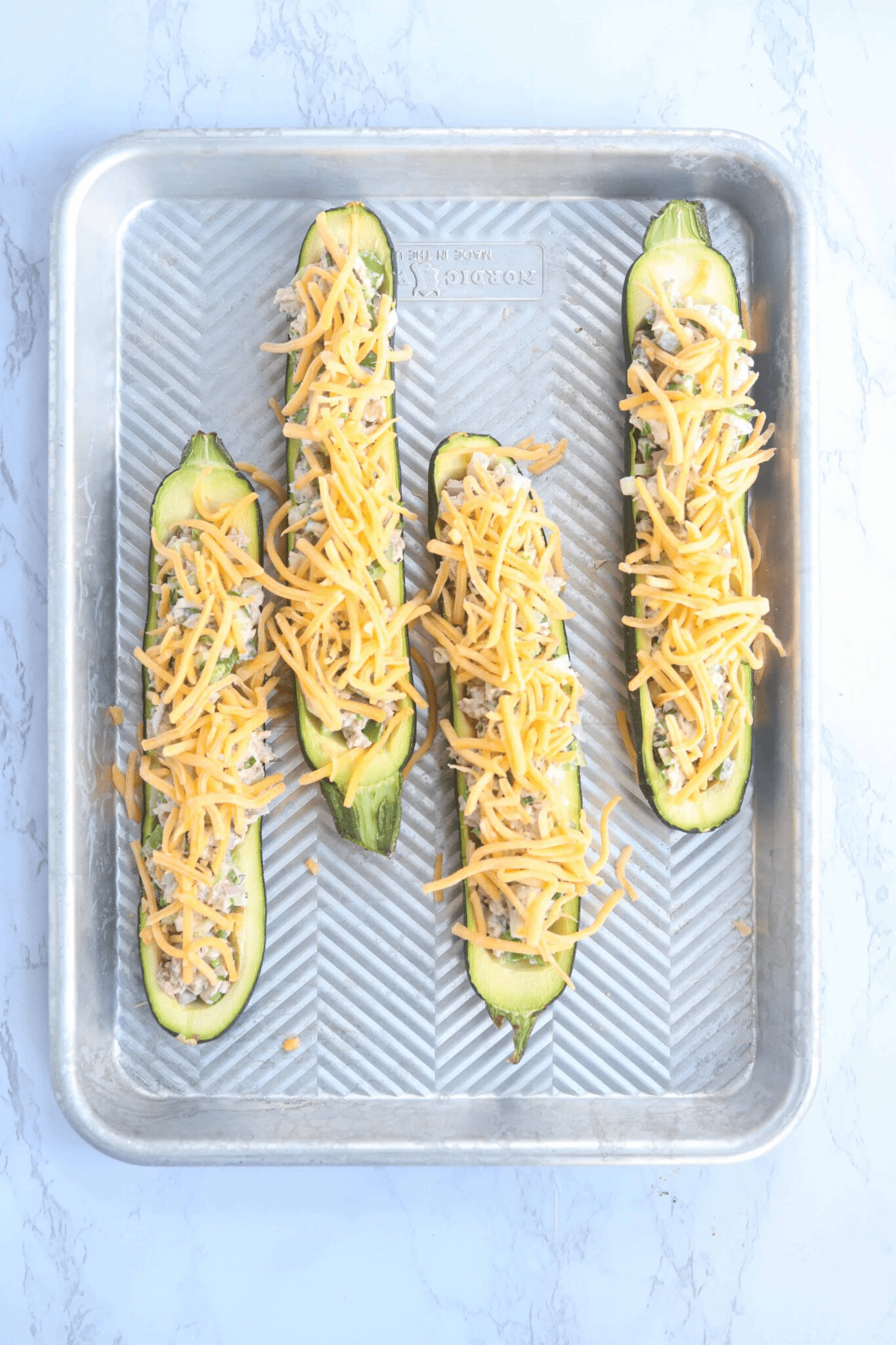 four zucchini boats filled with tuna salad and grated cheese on a baking tray.