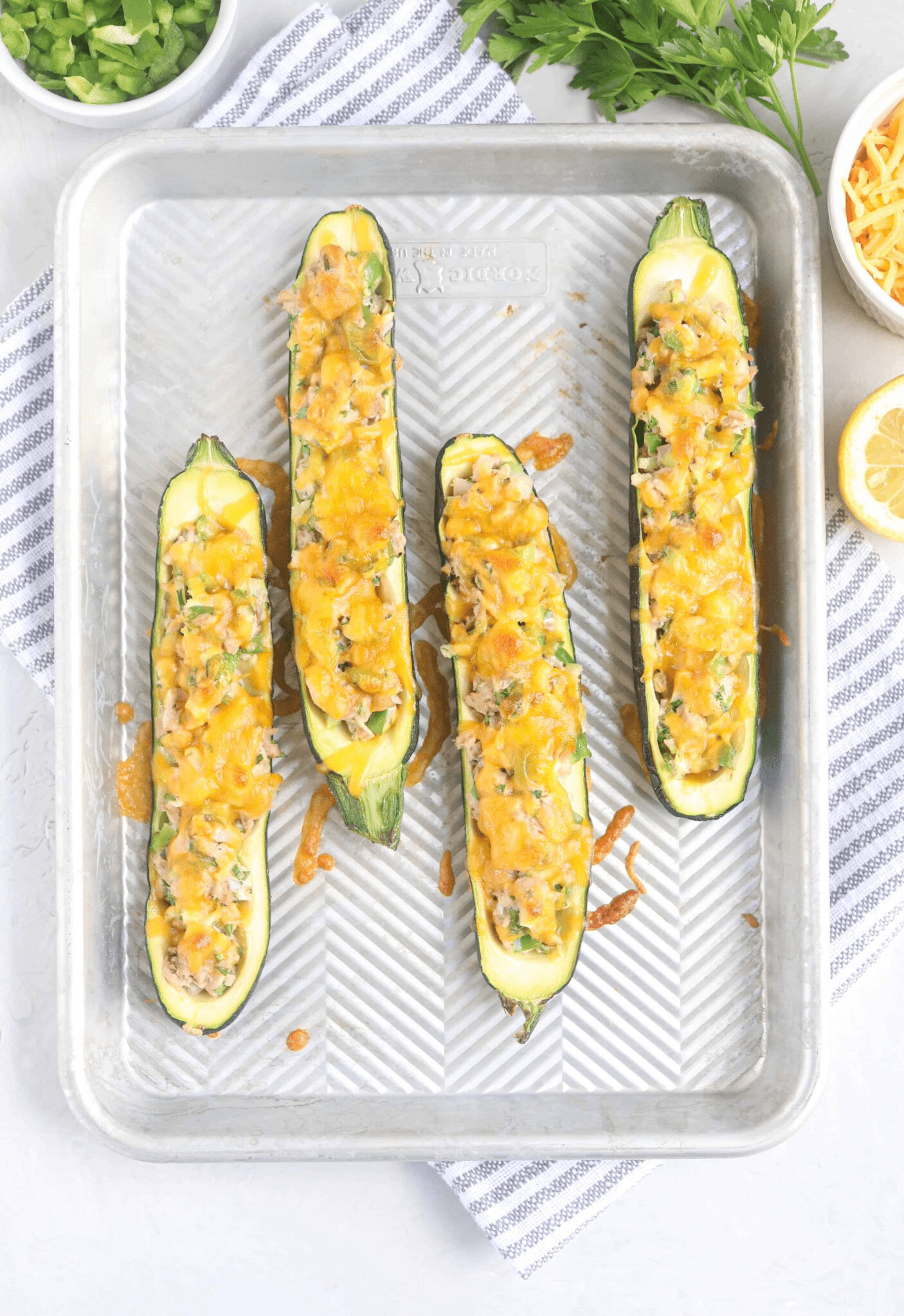 four zucchini boats filled with tuna salad and melted cheese on a baking tray.