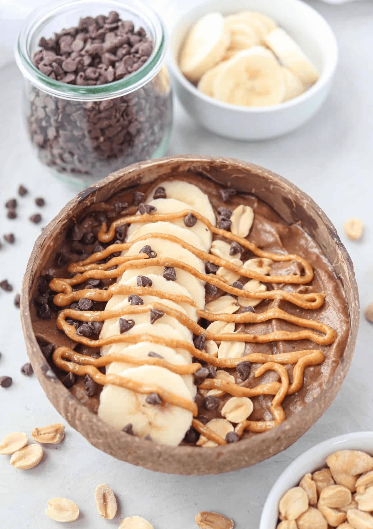 snickers smoothie bowl topped with sliced banana, peanuts, mini chocolate chips and peanut butter swirl in a natural coconut shell.