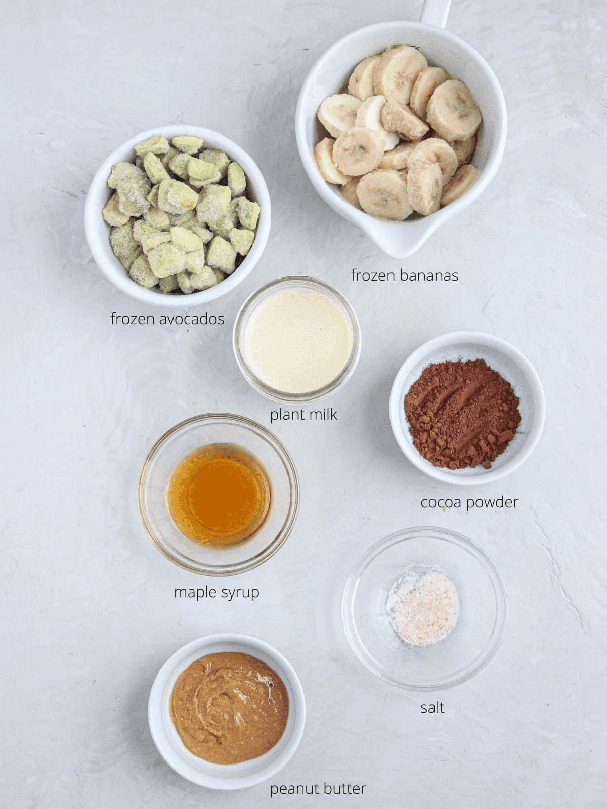 ingredients for making snickers smoothie bowl in small containers on gray surface with captions. 