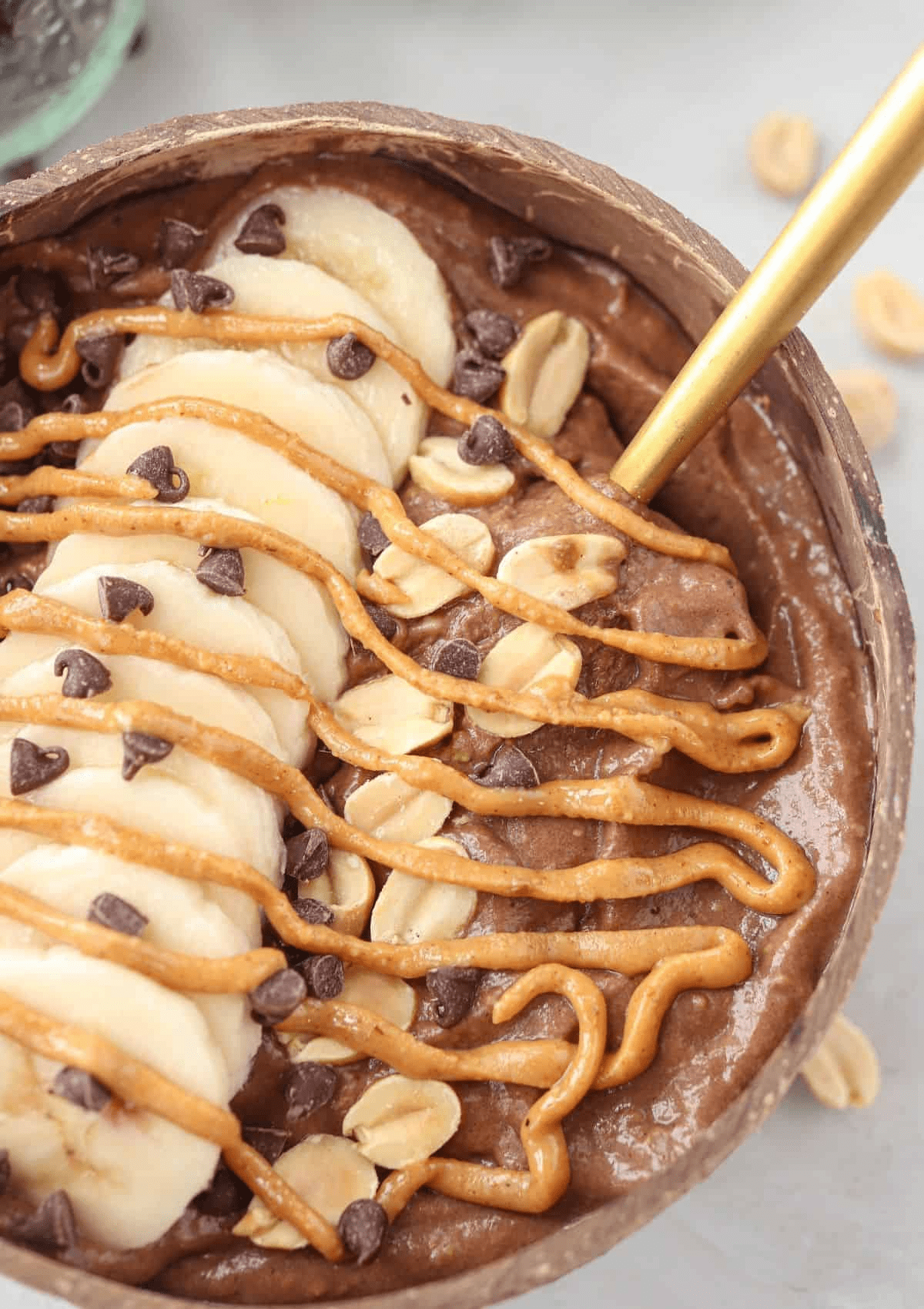 snickers smoothie bowl topped with sliced banana, peanuts, mini chocolate chips and peanut butter swirl in a natural coconut shell.
