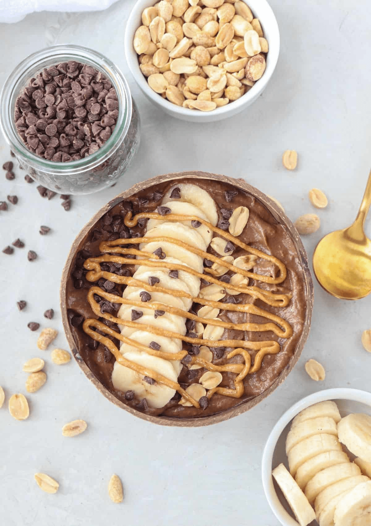 snickers smoothie bowl topped with sliced banana, peanuts, mini chocolate chips and peanut butter swirl in a natural coconut shell.