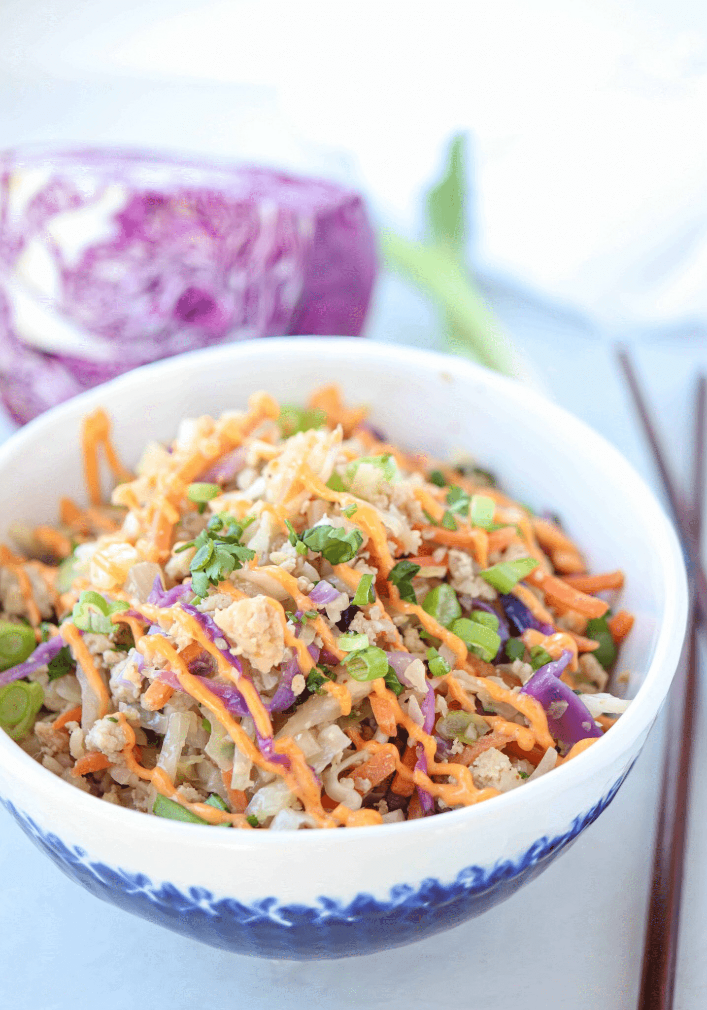 white and clue bowl with meat, veggies, sriracha mayo and cilantro on light gray surface.