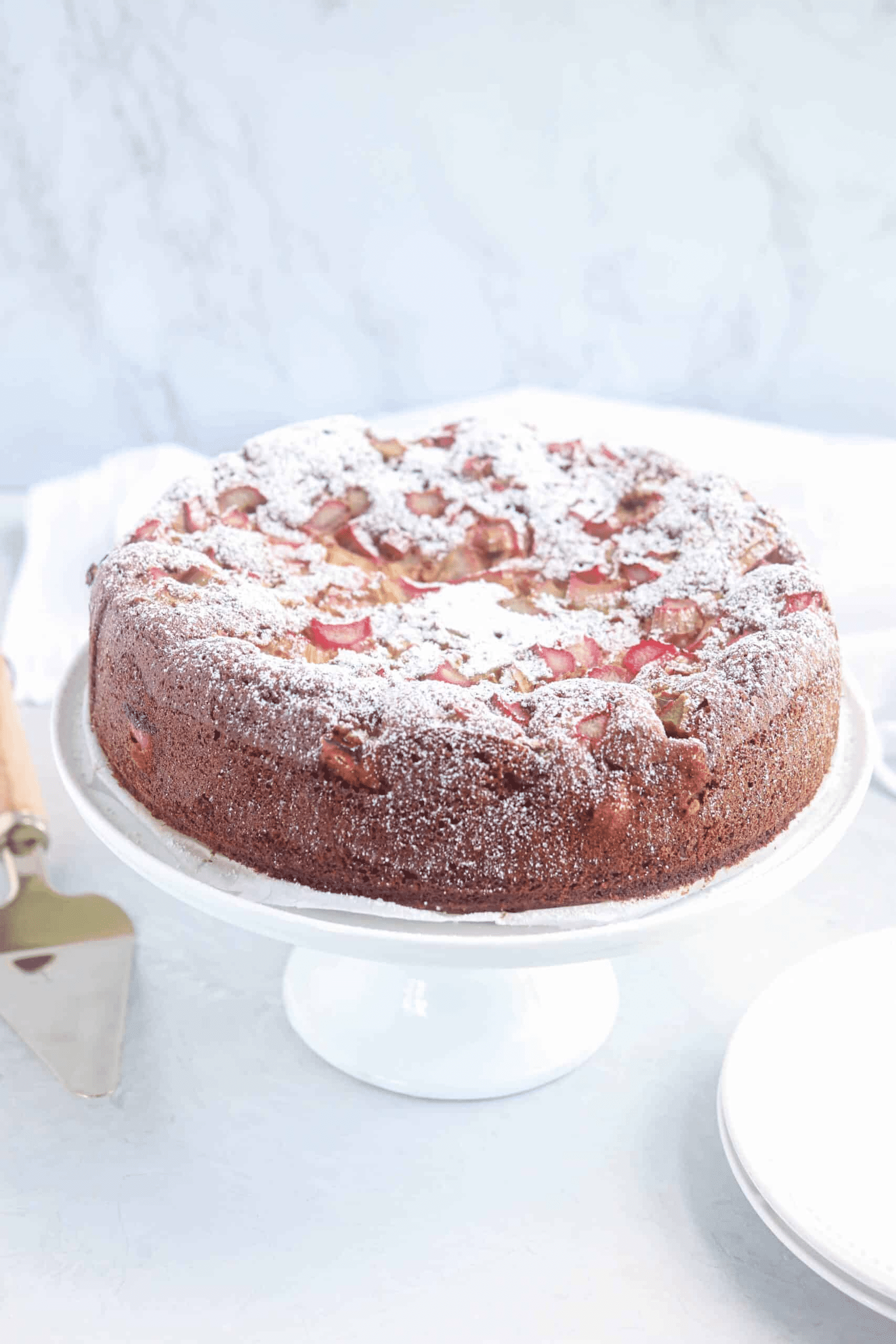 rhubarb cake dusted with powdered sugar on a white stand.