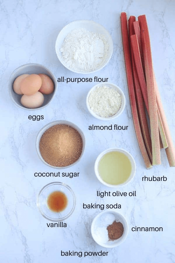 ingredients for rhubarb cake on white marble surface with captions. 