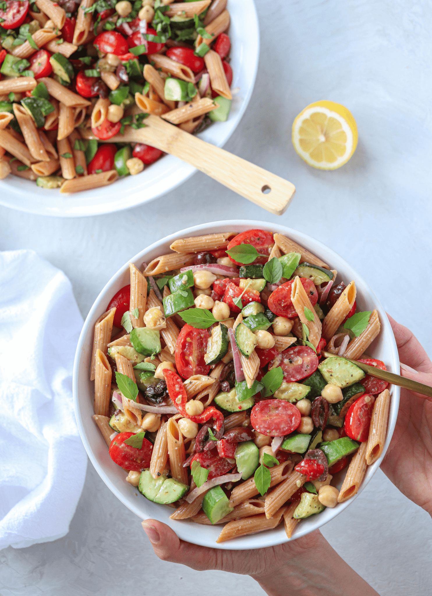 pasta salad with vegetables in a white bowl held by two hands.