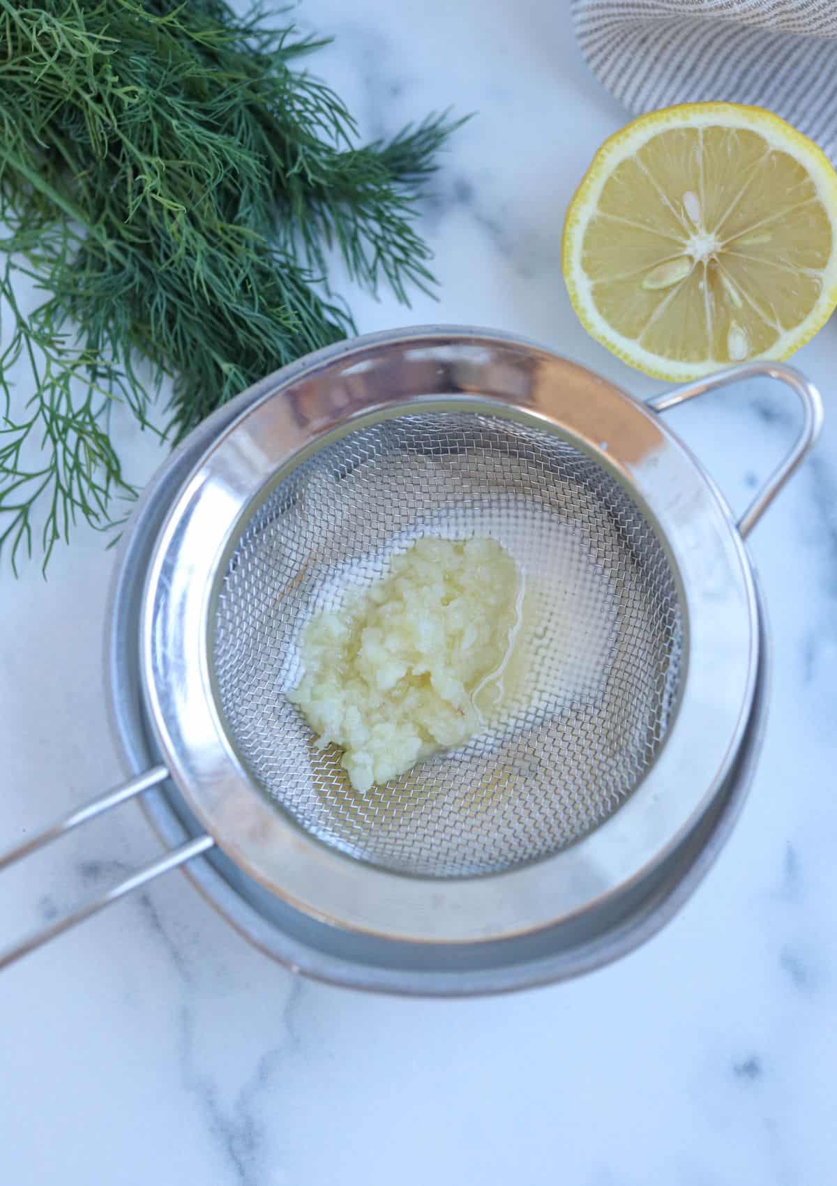 pressed garlic on a fine mesh strainer over a gray bowl. 