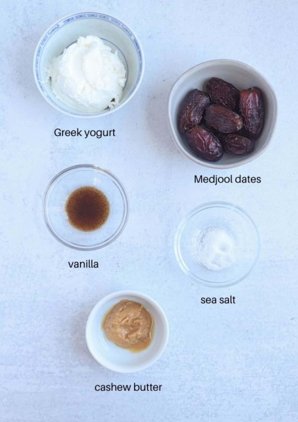 healthy caramel yogurt dip ingredients in small round containers on light gray surface.