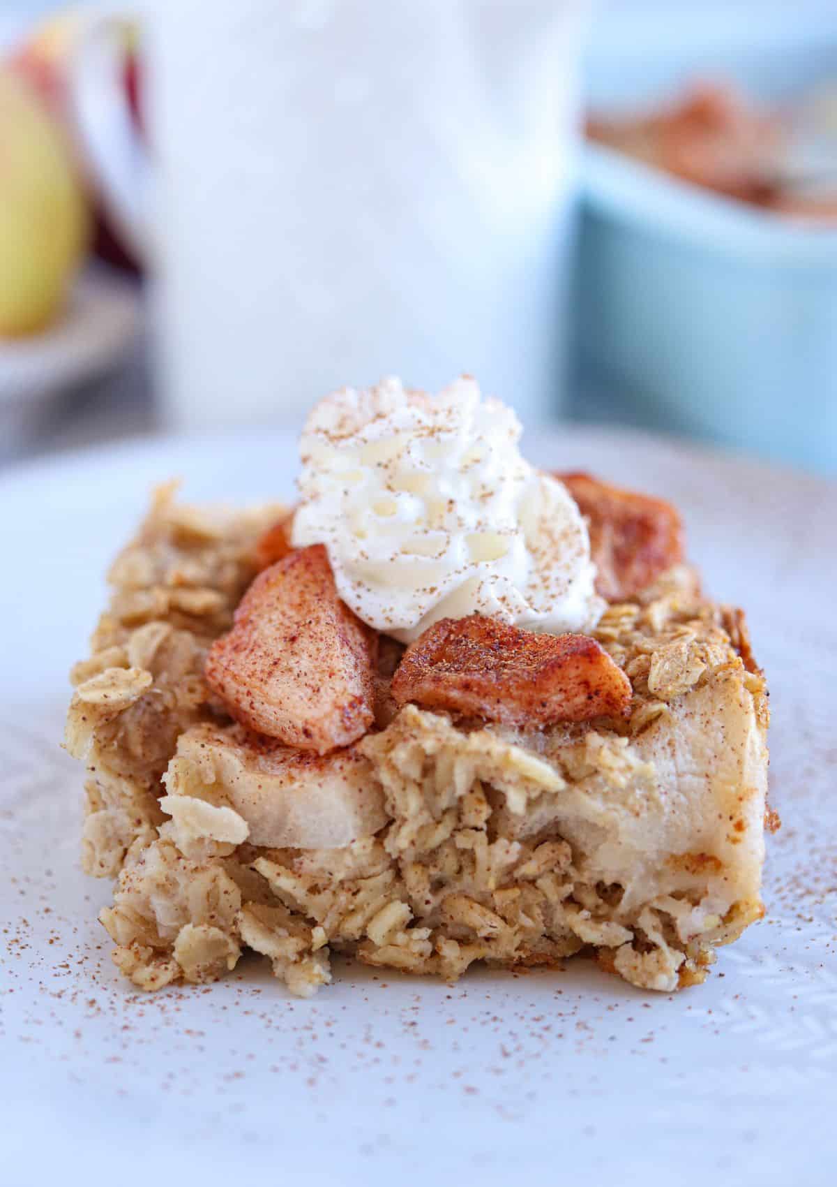 apple pie baked oatmeal square topped with cooked apples, whipped cream, cinnamon and maple syrup.