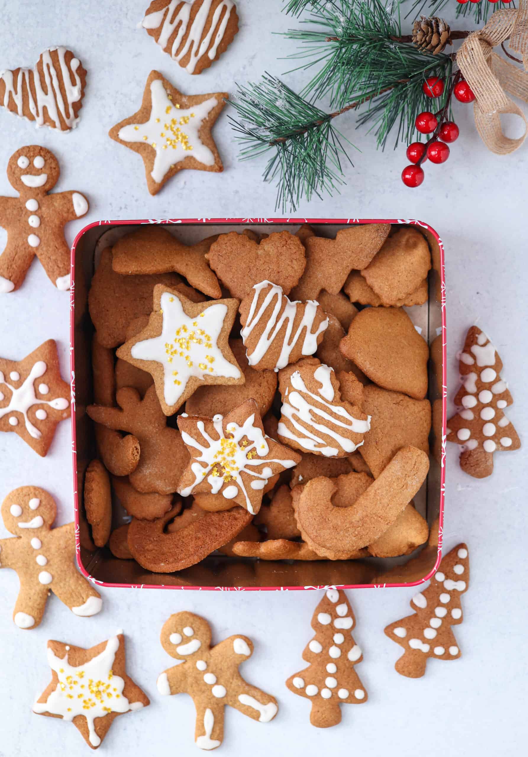 Polish gingerbread cutout cookies with white  royal icing and golden star sprinkles in a red square tin and on light gray surface. 