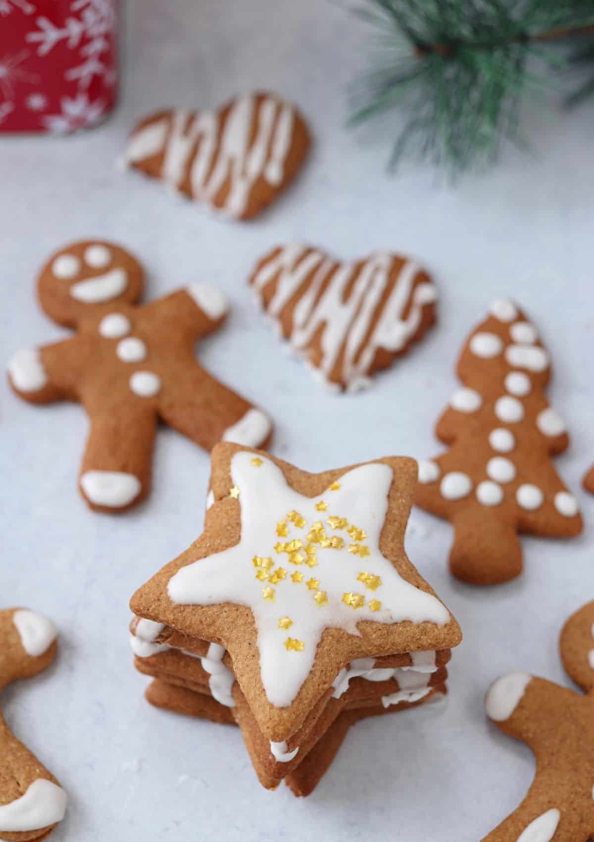 Polish gingerbread cutout cookies with white  royal icing and golden star sprinkles on light gray surface. 