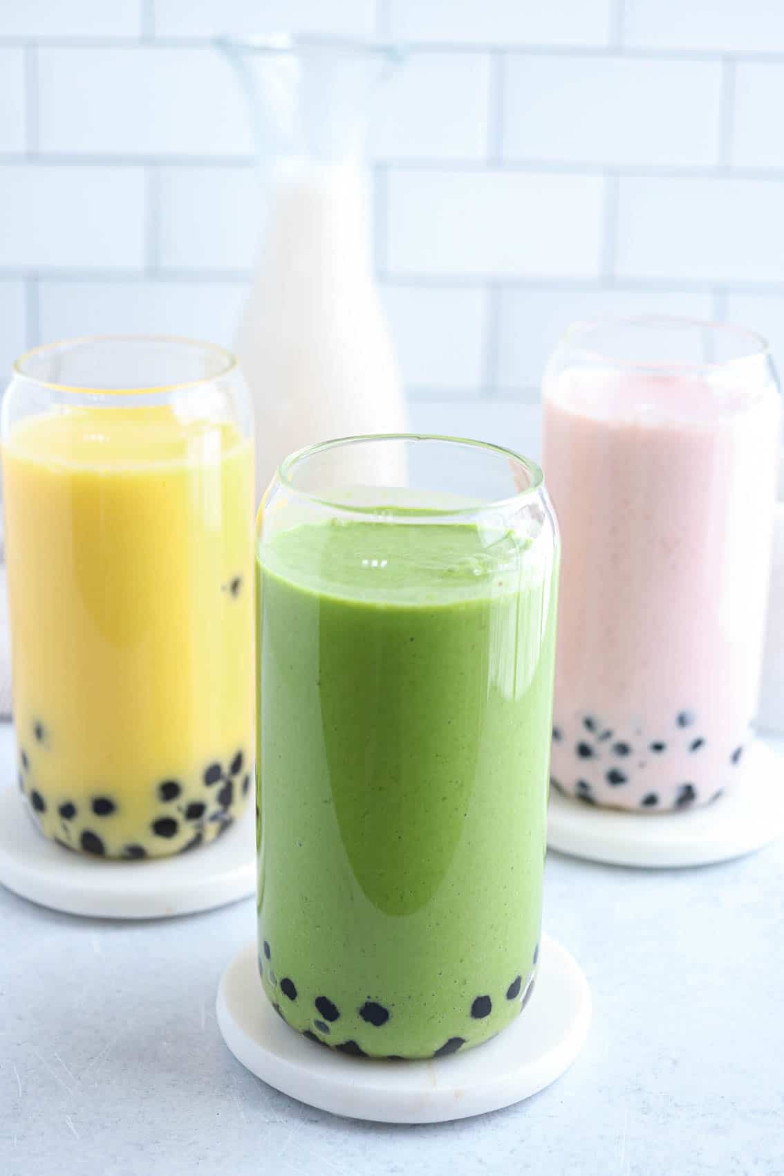 three boba smoothies: yellow, pink and green in beer can shaped glasses.