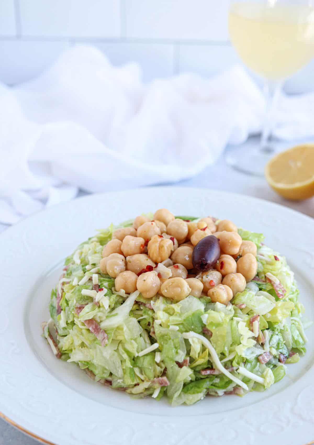 chopped salad with salami, mozzarella and marinated chickpeas on top on a white plate.