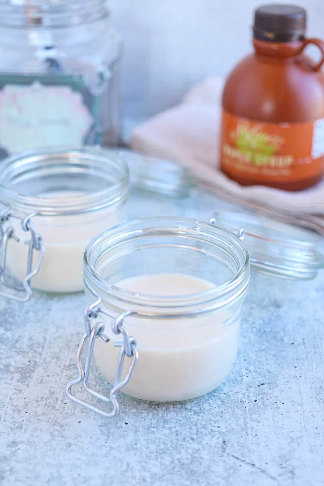 two glass jars with oat milk on gray surface.