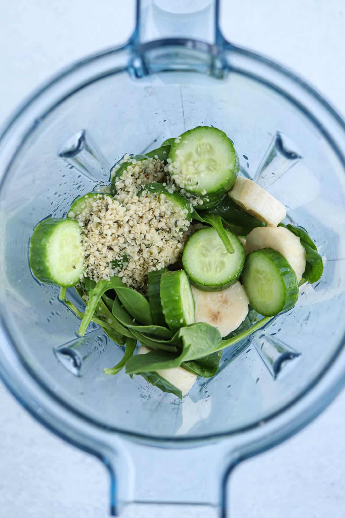 cucumbers, spinach, banana and hemp seeds in a blender before blending into a smoothie.