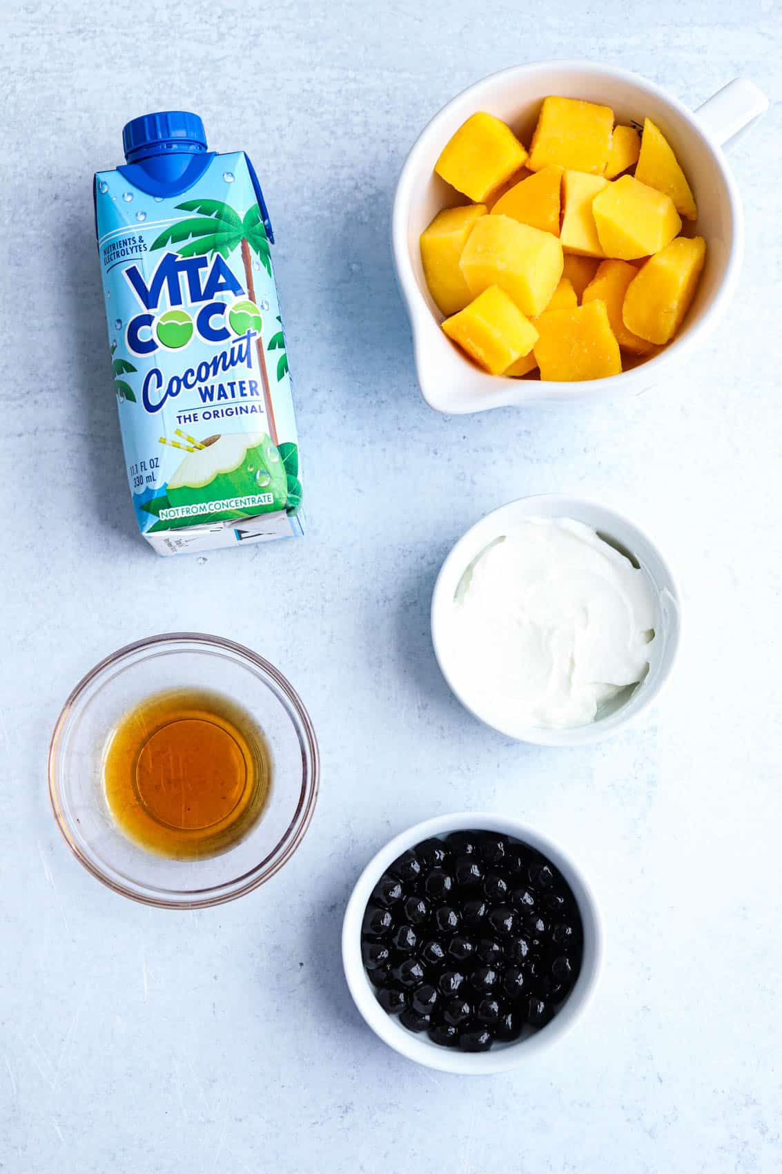ingredients for a mango boba smoothie in containers on light gray surface. 