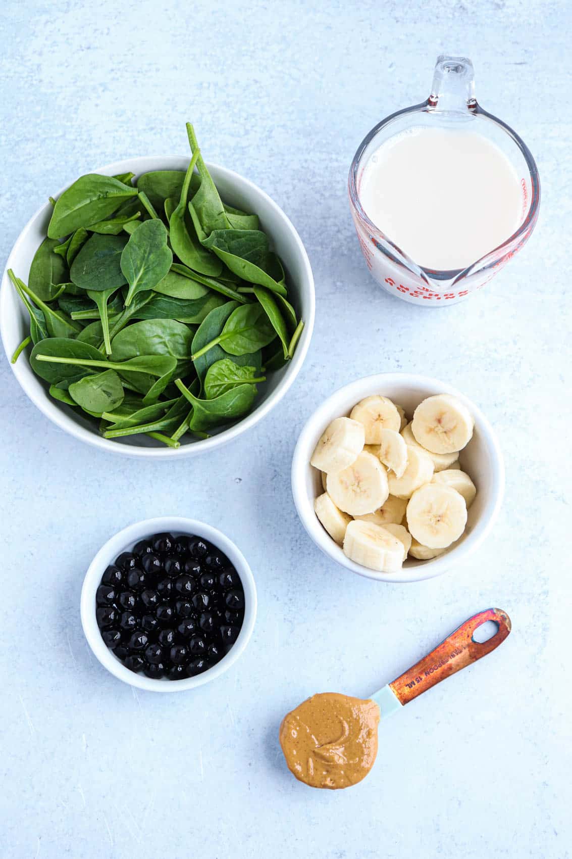 ingredients for a green boba smoothie in containers on light gray surface. 