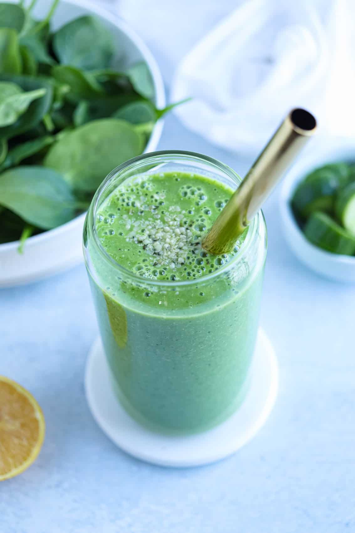 bright green spinach cucumber smoothie in a tall glass with a golden wide straw. 