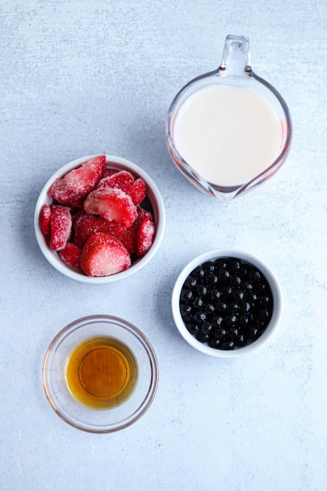 ingredients for a strawberry boba smoothie in containers on light gray surface. 