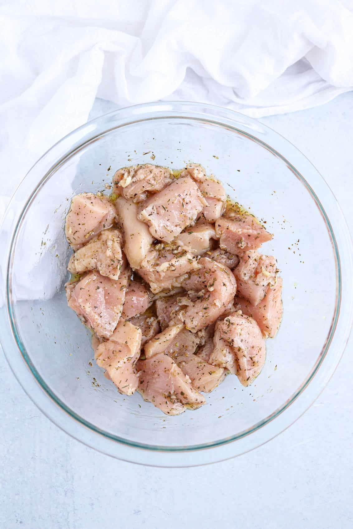 chicken breast pieces in marinade in a glass bowl.