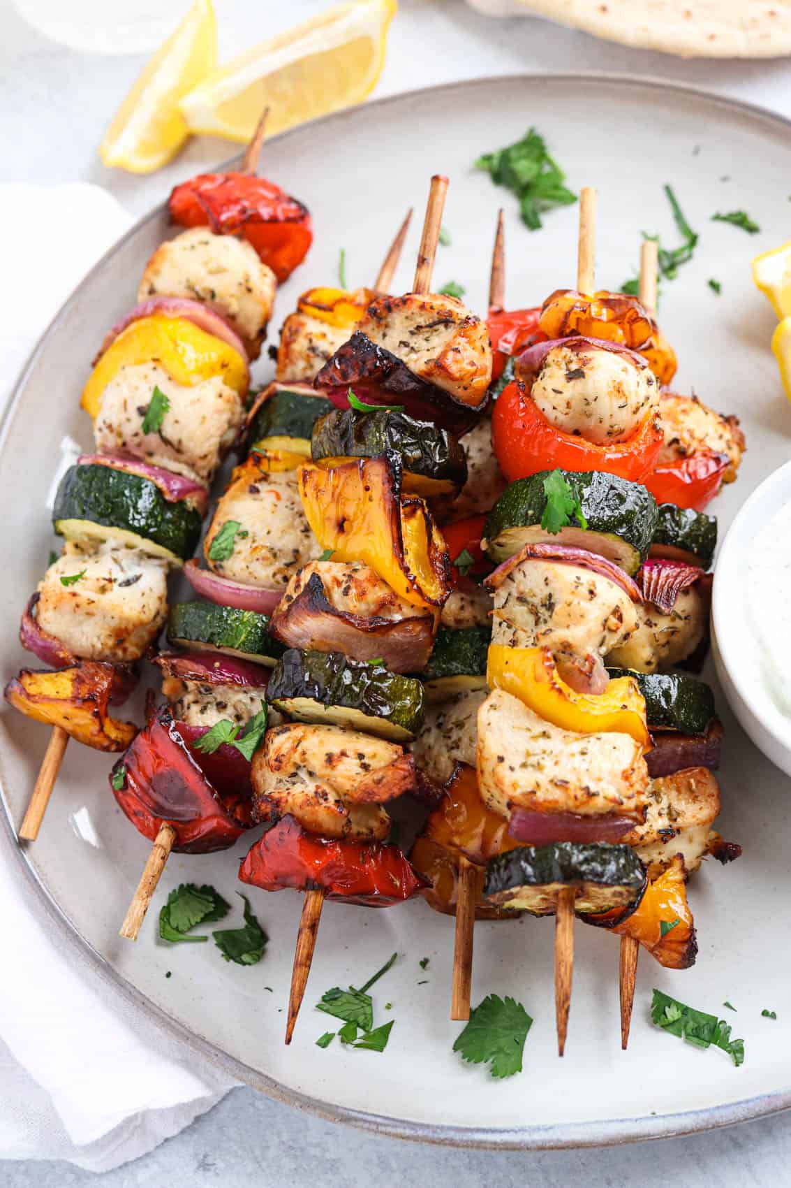 chicken and vegetable kebabs on wooden skewers stacked on a gray plate with a side of ranch dip.