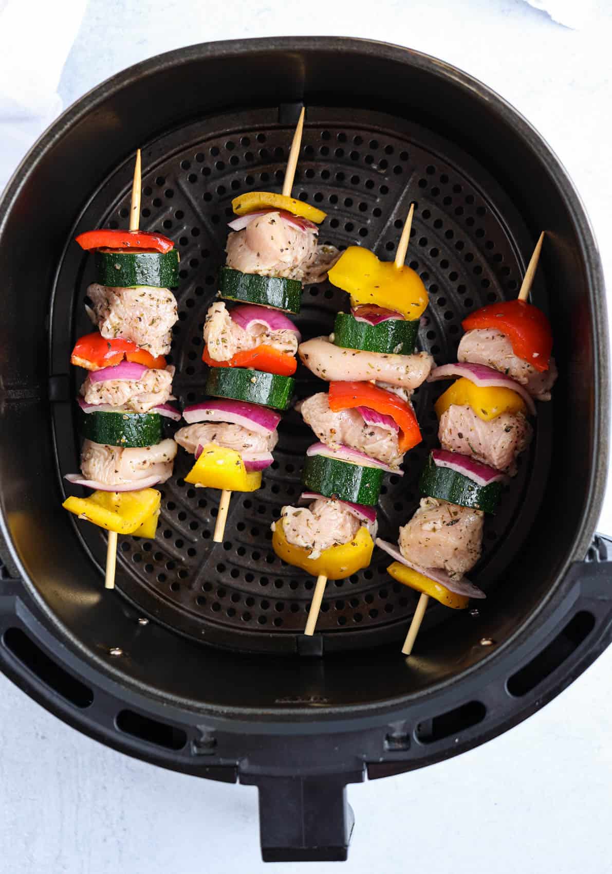 chicken and vegetables skewers in an air fryer basket, before cooking.