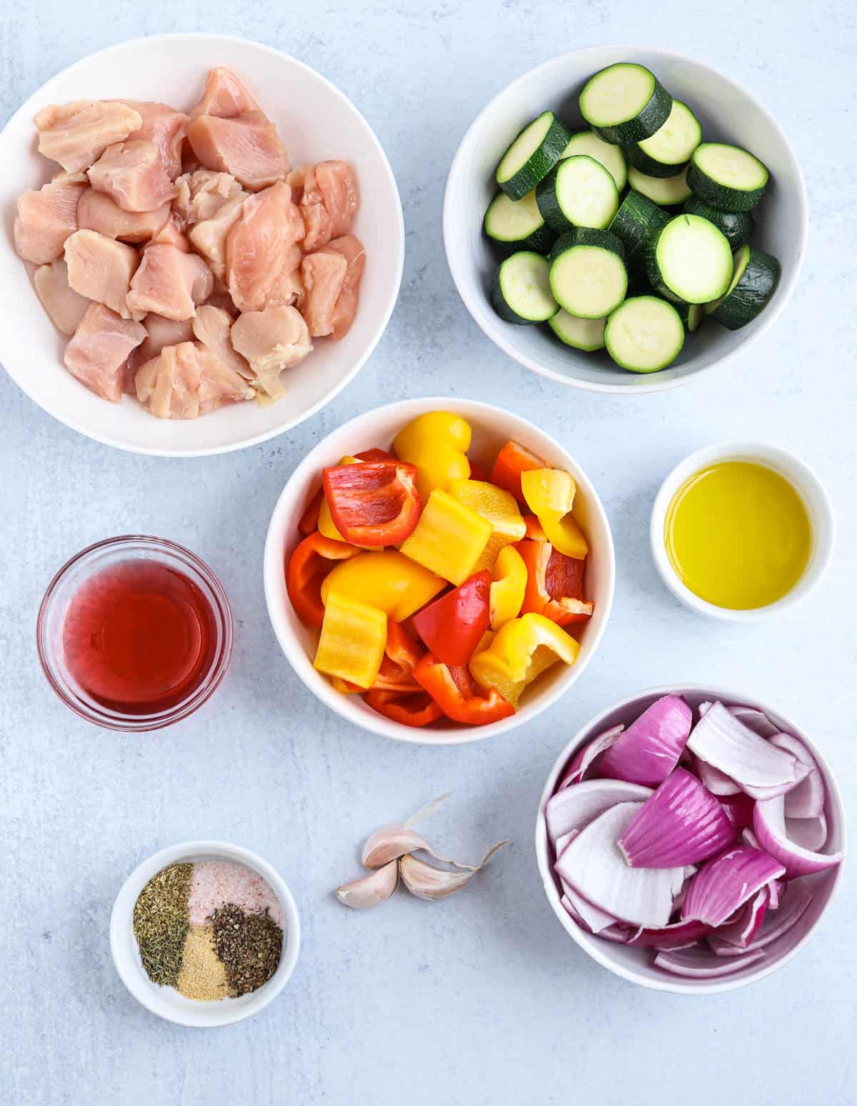 ingredients for making chicken kebabs in white bowls on gray surface. 