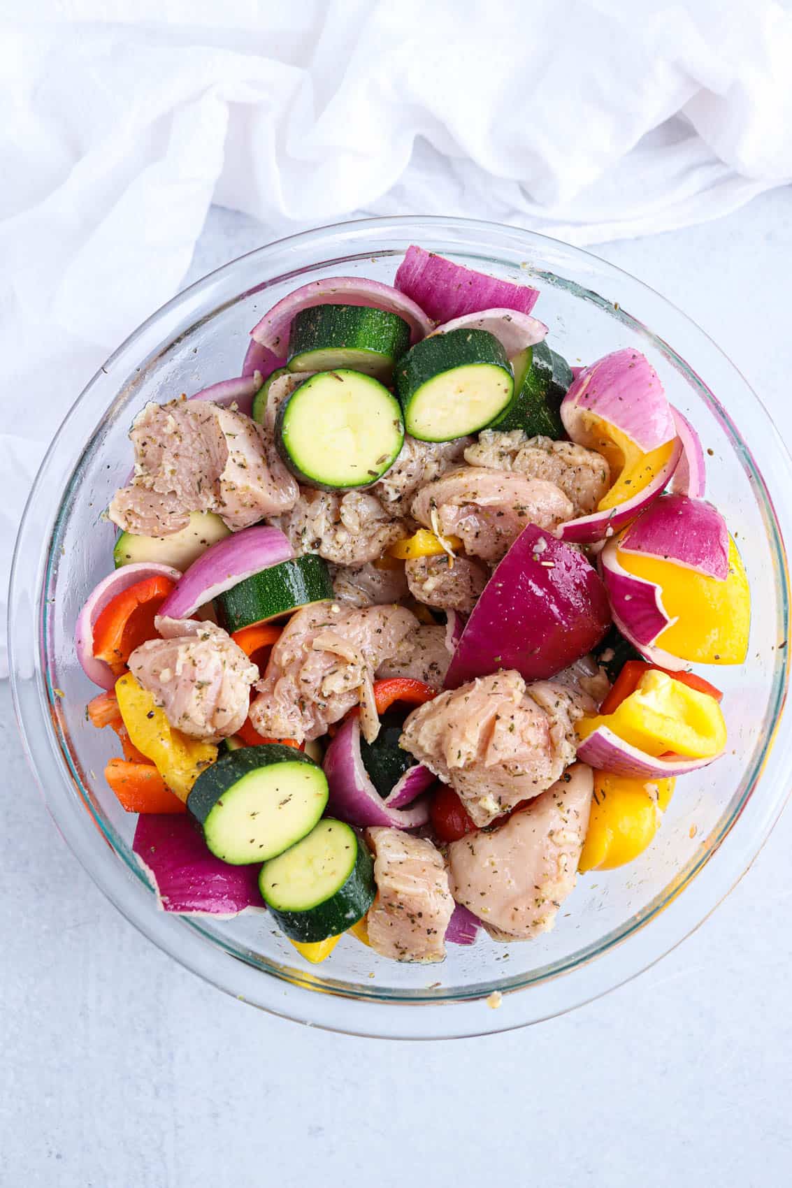 chicken pieces and cut up veggies in marinade in a glass bowl.