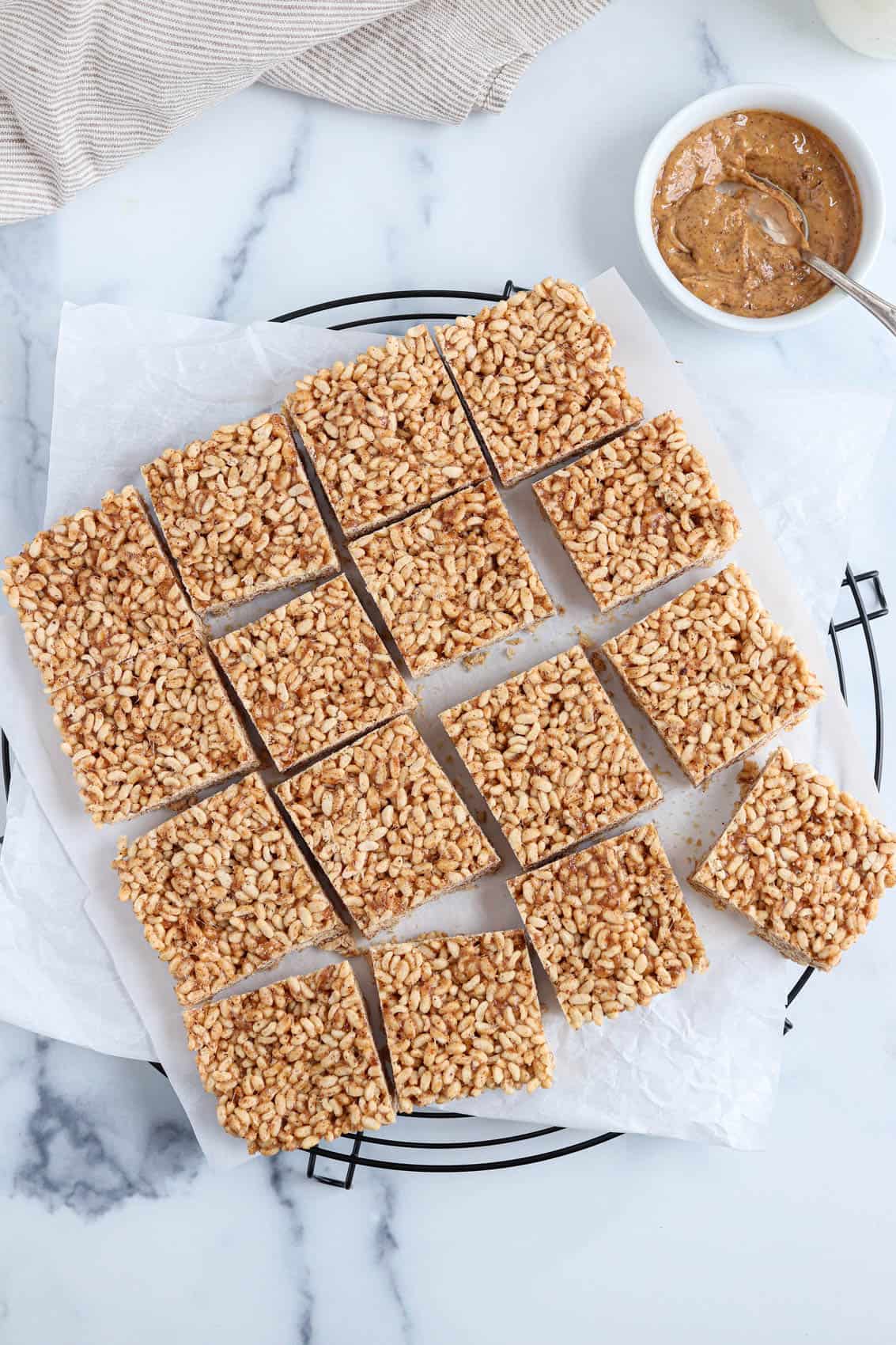 healthy rice krispie treat squares on white paper on top of a black cooling rack. 