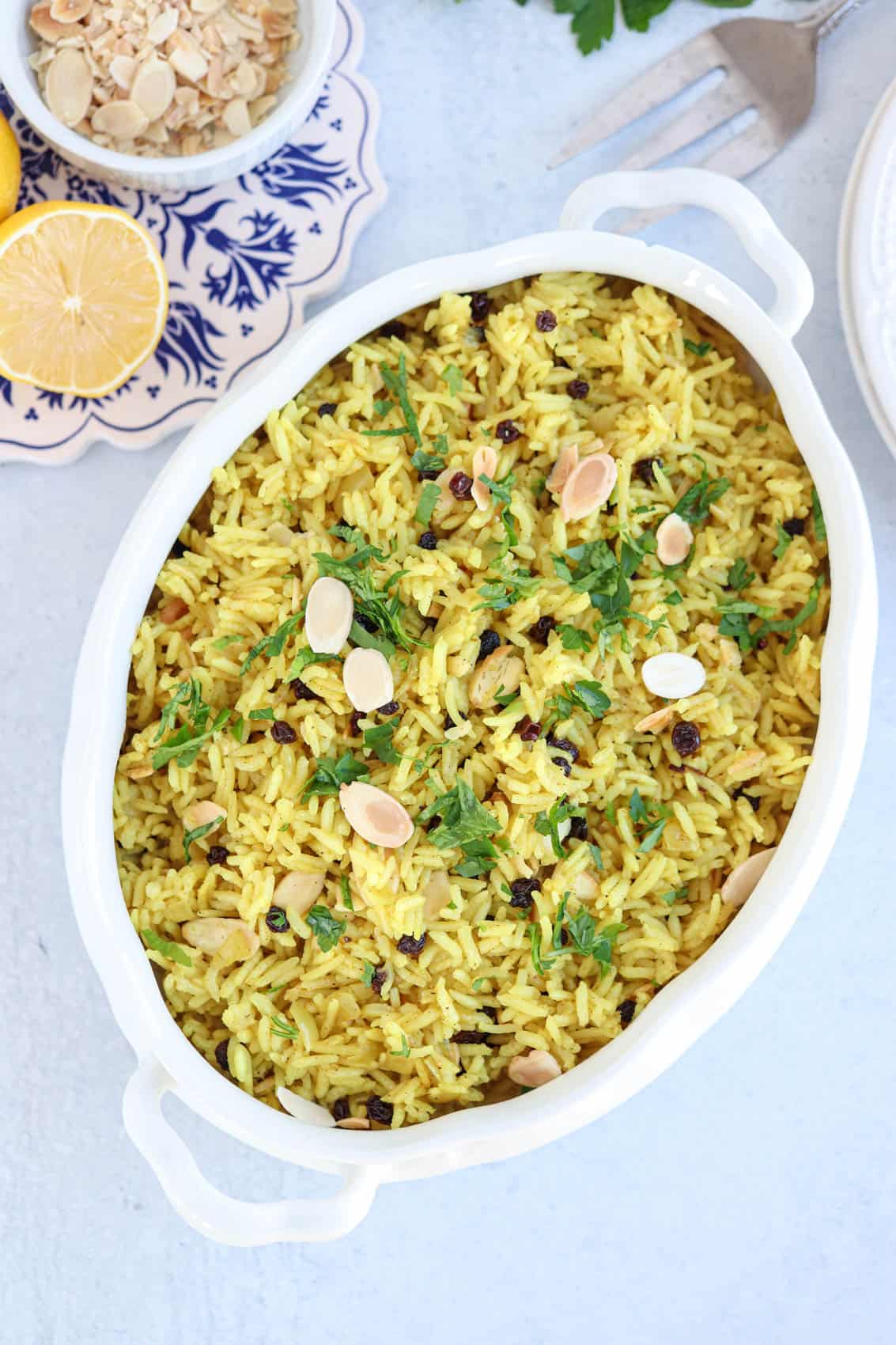 yellow rice with sliced almonds, currants and fresh parsley in a white oval serving dish.