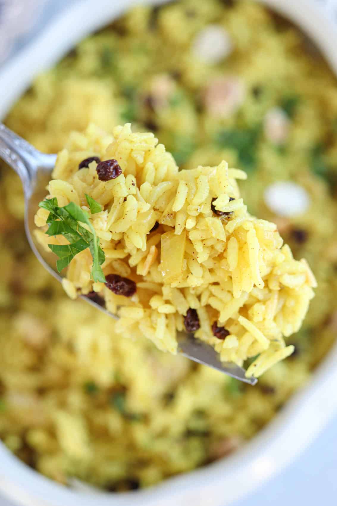 close up of yellow rice pilaf with currants and almonds on a fork.