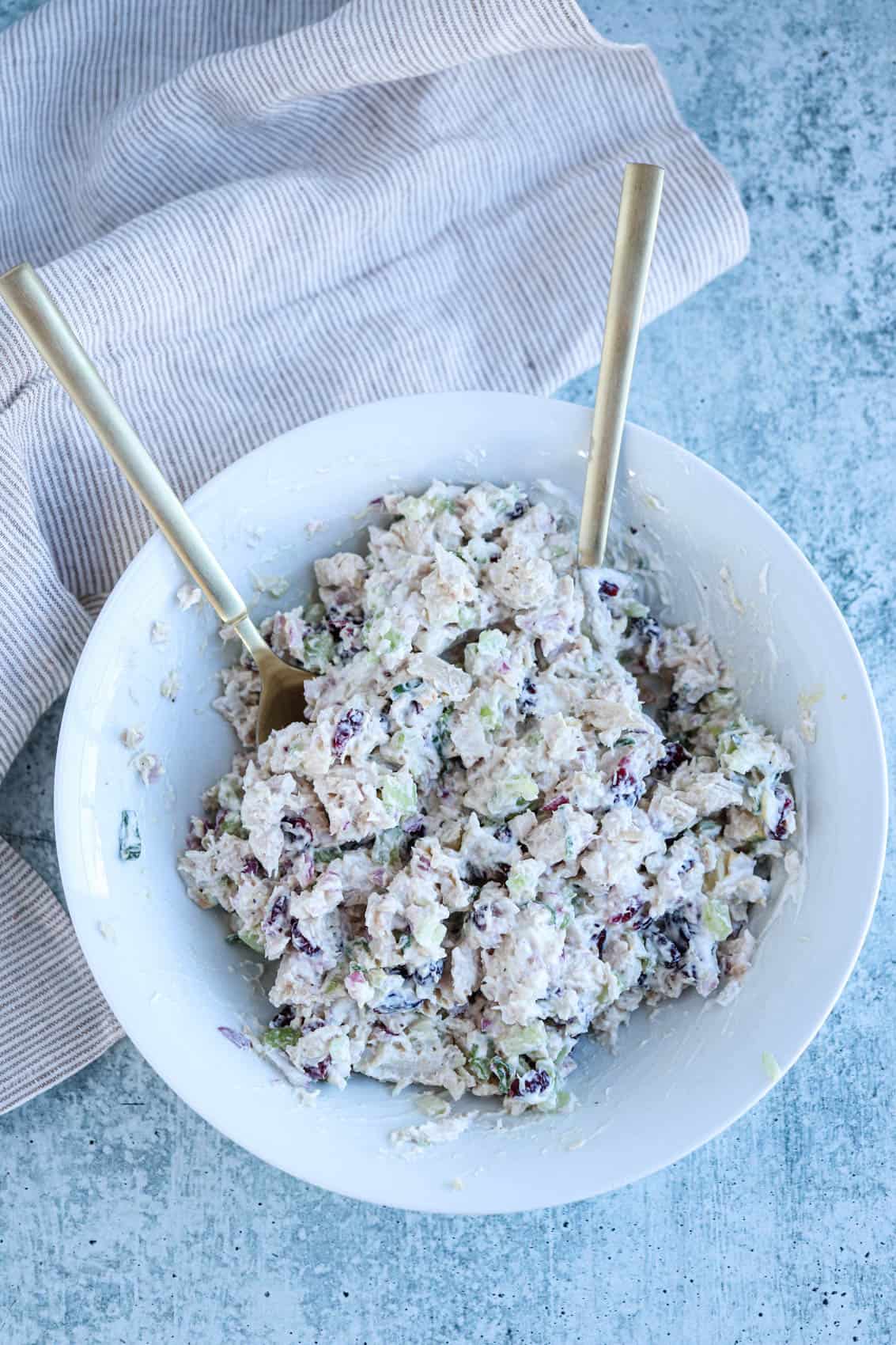 mixing creamy chicken salad in a white bowl with two spoons. 
