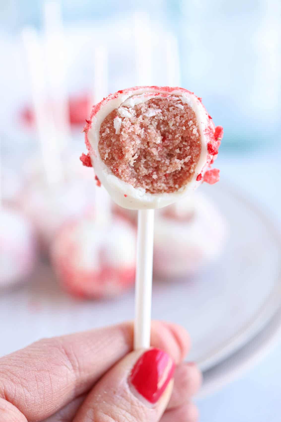 strawberry cake pops in w hite chocolate with a bite taken out, held by a hand.
