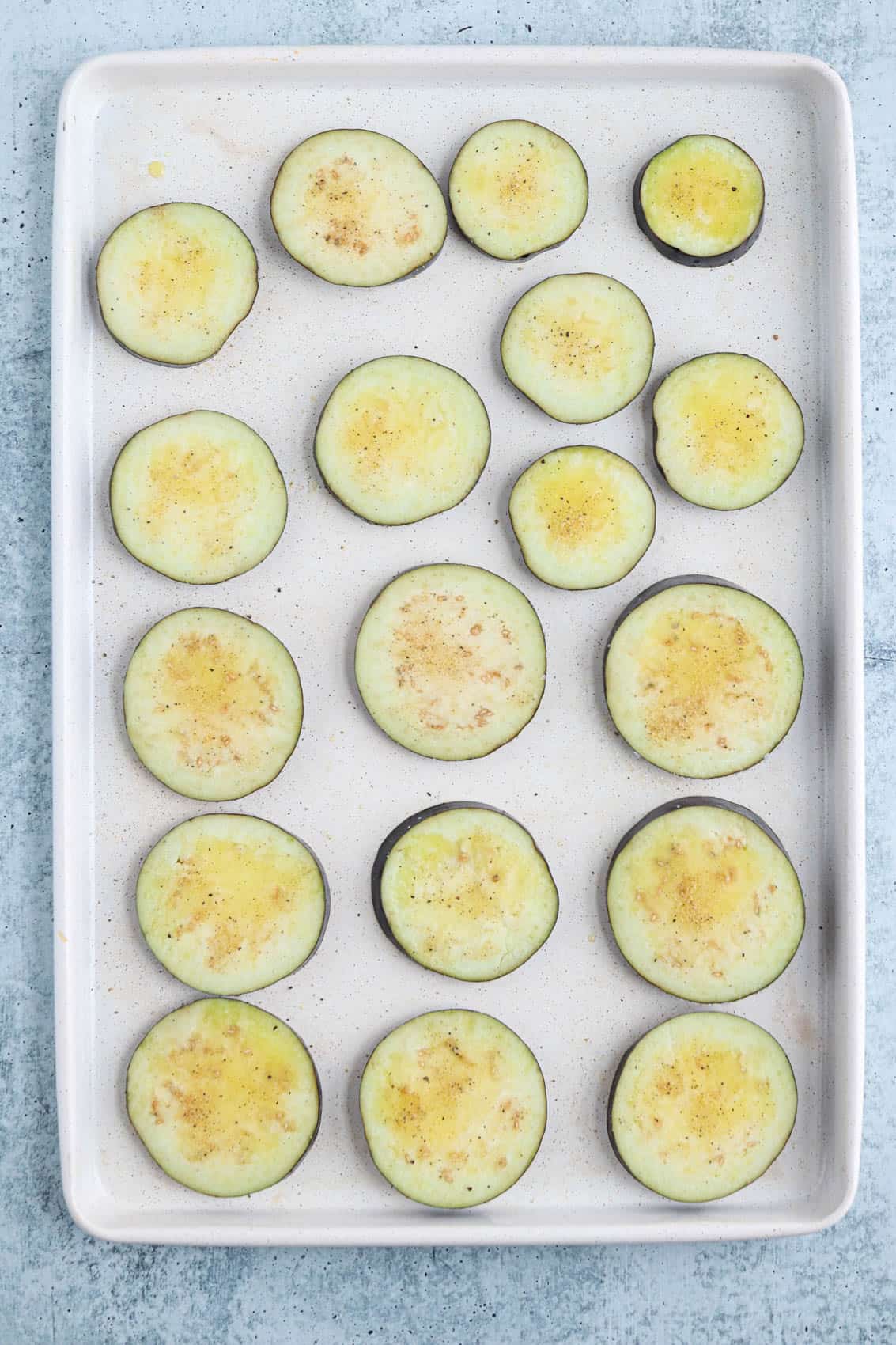 raw eggplant slices seasoned and brushed with oil on paper towel lined paper towels.