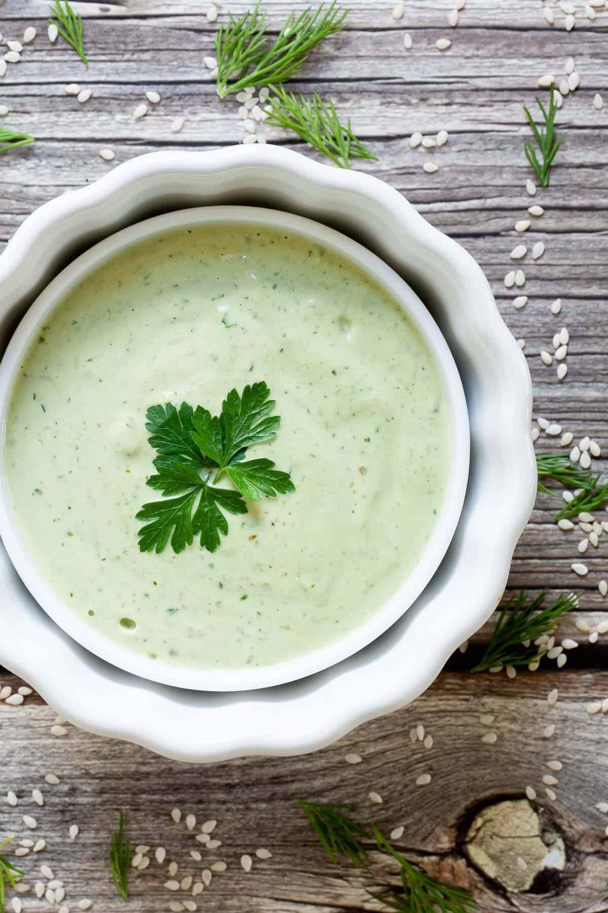 green creamy sauce in a white dish on a wooden board.
