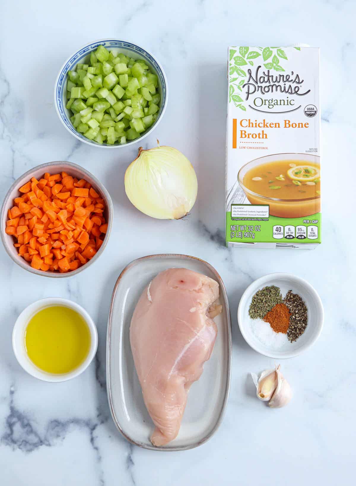 ingredients for making bone broth chicken soup in containers oon white marble surface. 
