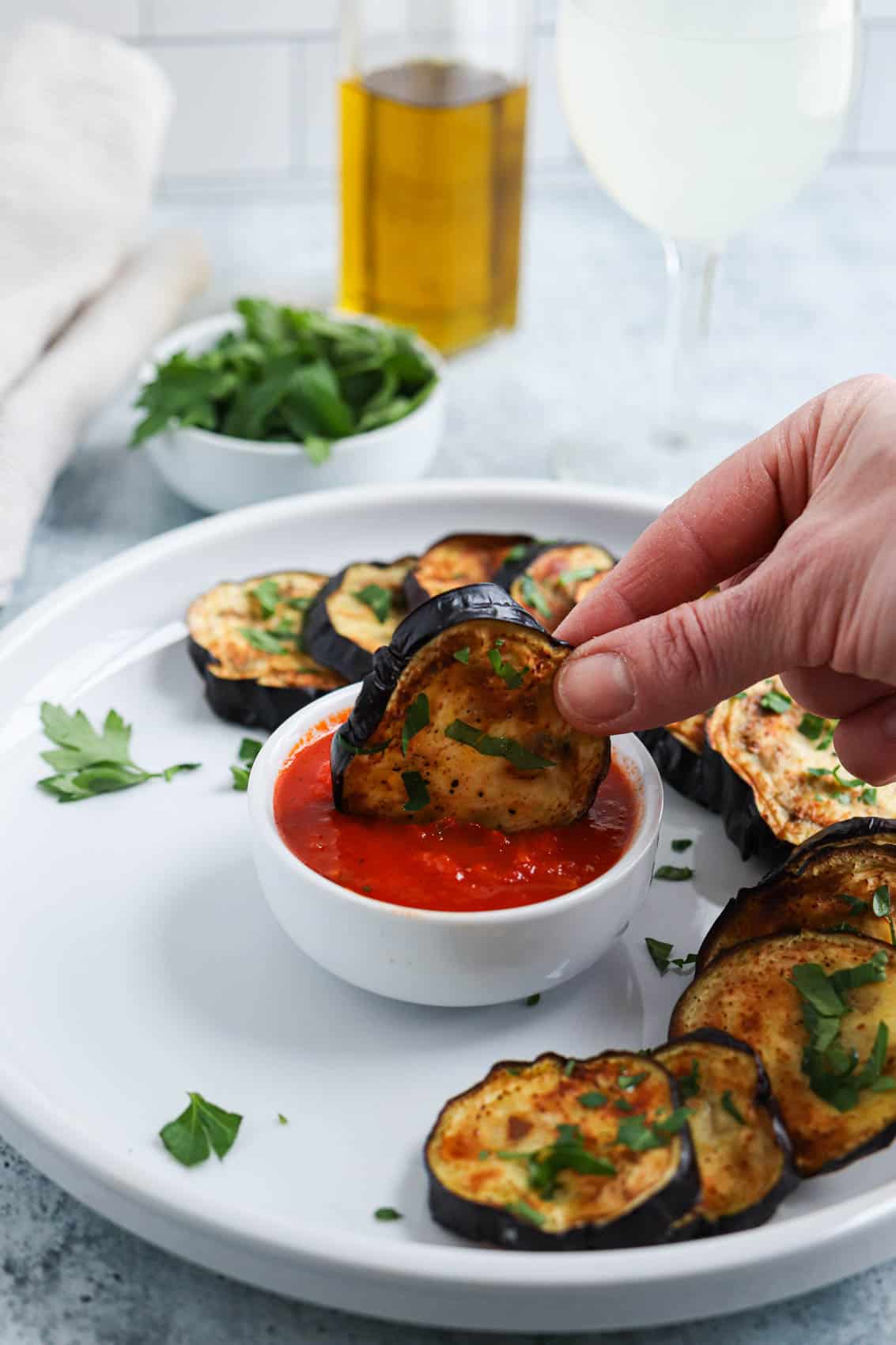 air fryer roasted eggplant slices on a white plate with a side of Marinara sauce, one slice being dipped in the sauce.