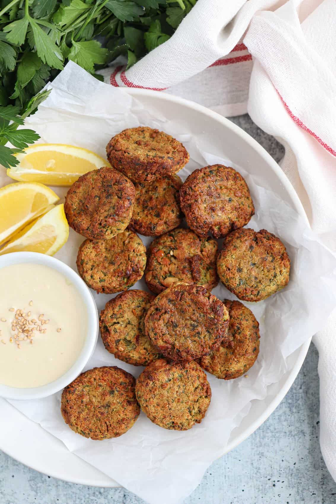 air fried falafel patties on a white plate on white wax paper with a side of tahini sauce.