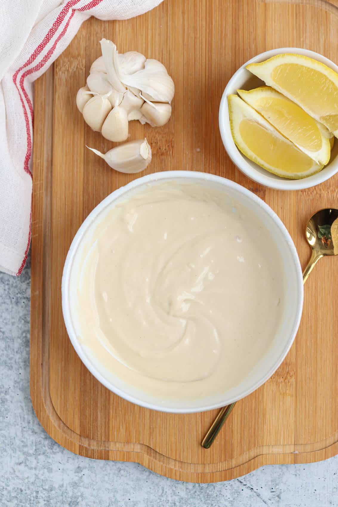 making lemon tahini sauce in a white bowl on a bamboo board.