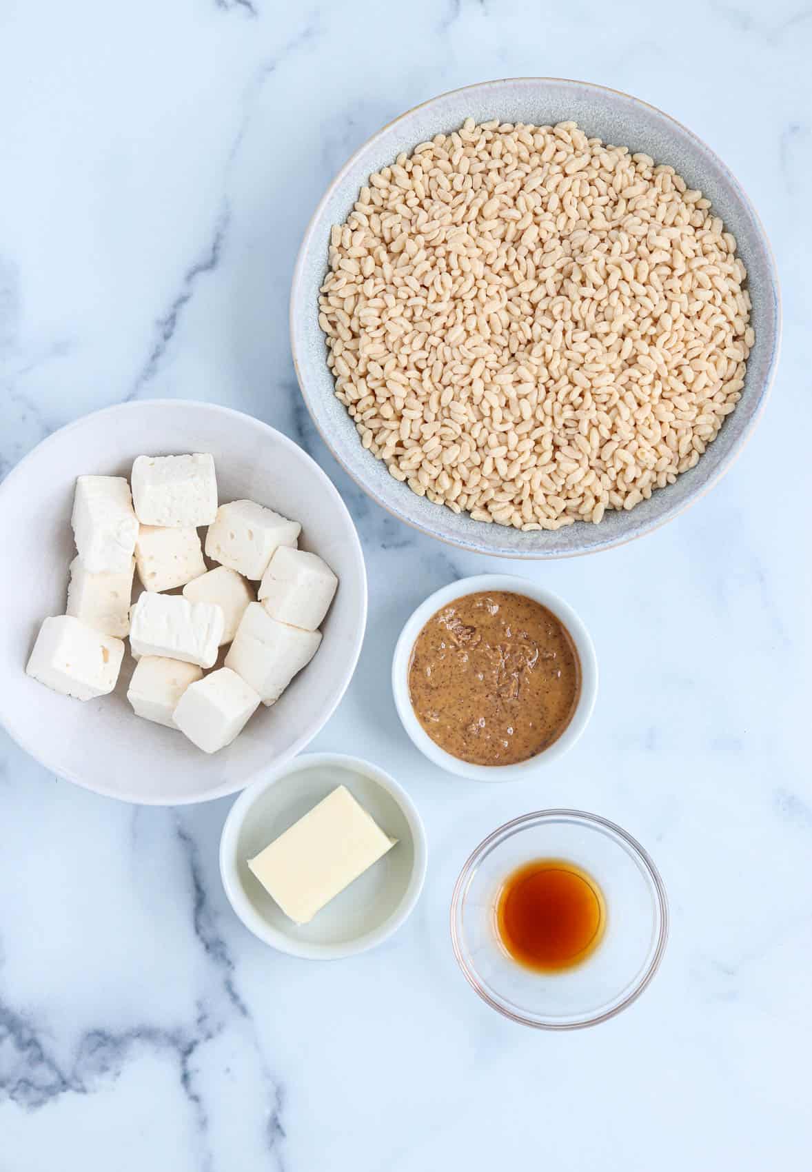 ingredients for making healthy rice krispie treats in round containers on white marble surface. 