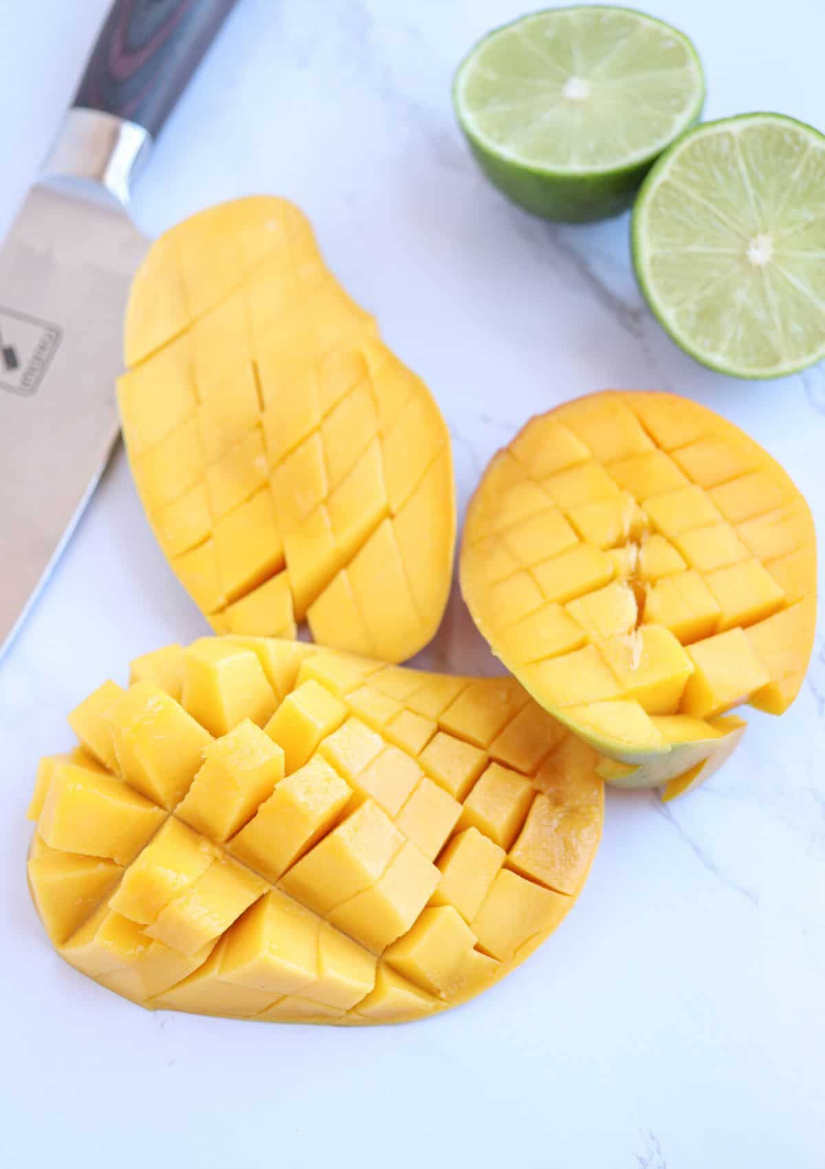 mango halves being cut into a dice on white marble surface, cut side up.