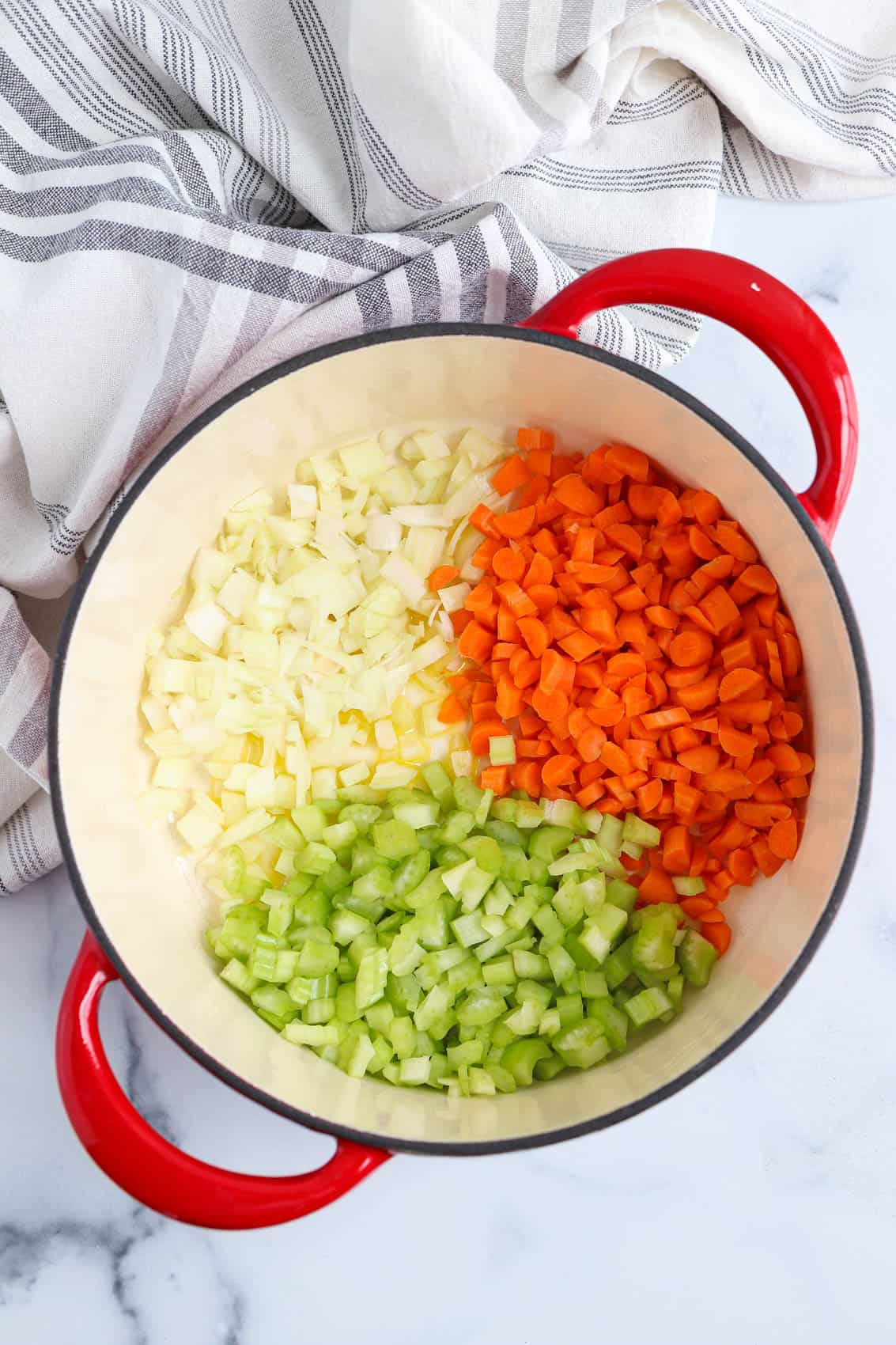 cooking carrots, onions and celery in a red dutch oven.