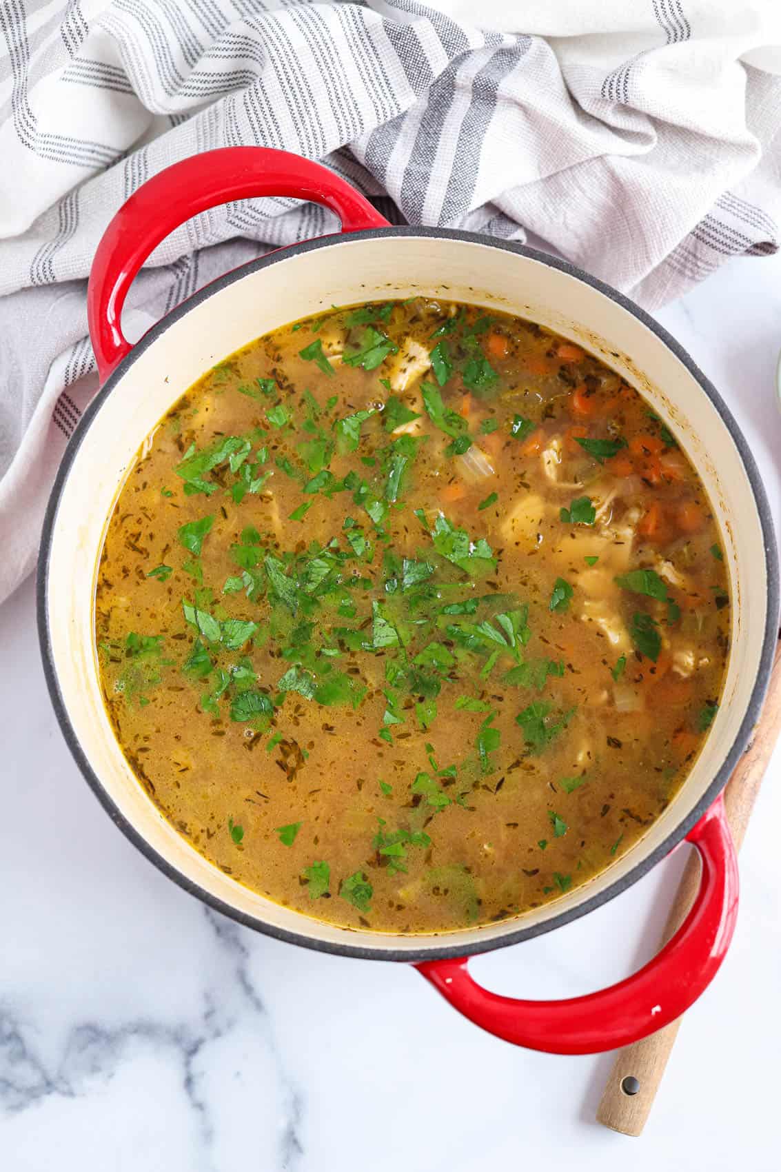 bone broth chicken soup sprinkled with fresh parsley in a red dutch oven.