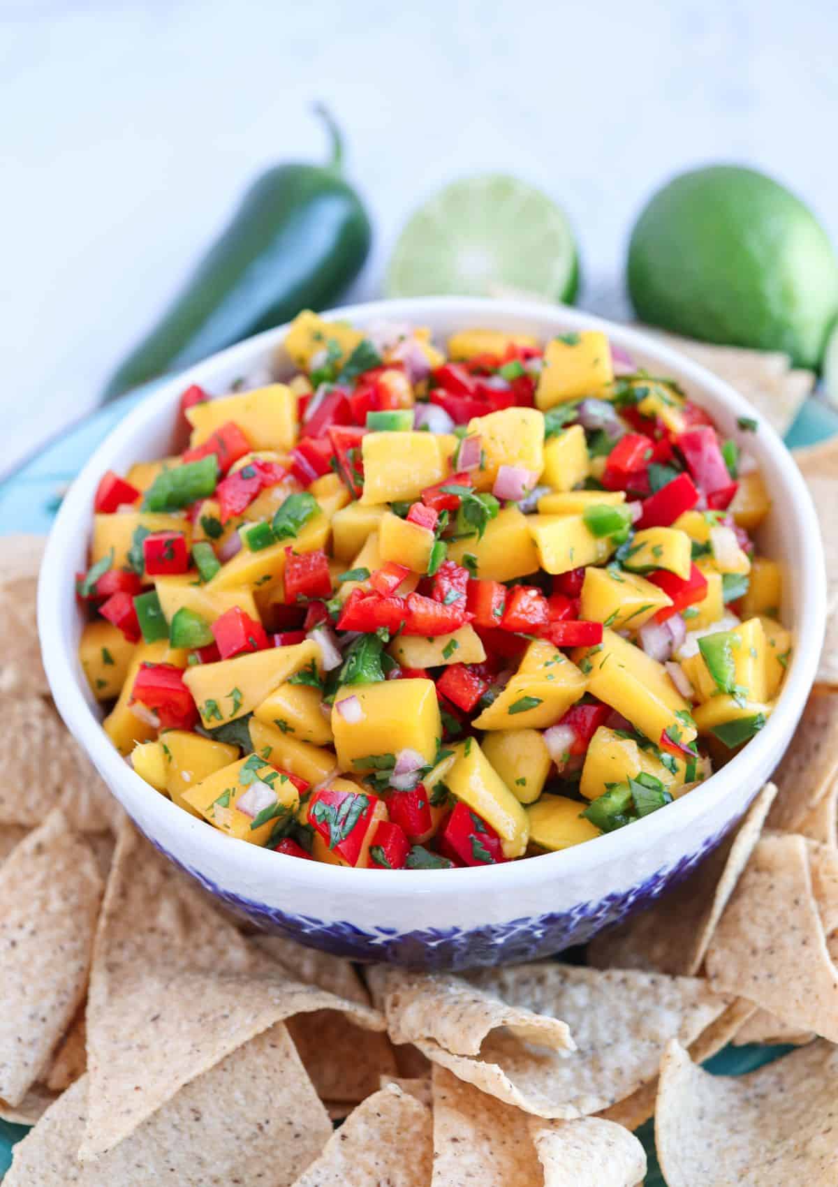 fresh mango pico de gallo in a white and blue bowl surrounded by tortilla chips.