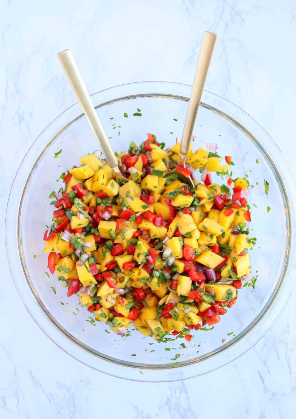 fresh mango pico de gallo in a glass bowl with two golden spoons.