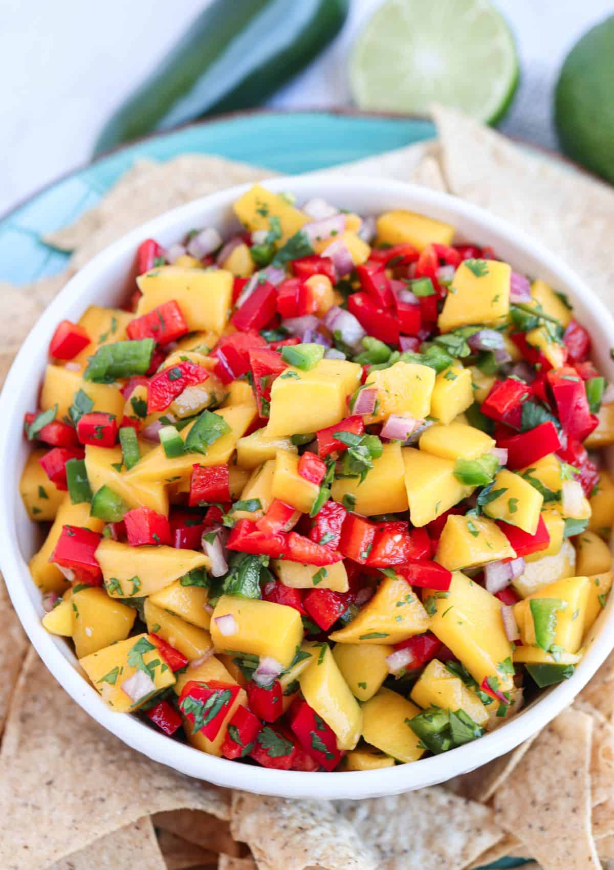 fresh mango pico de gallo in a white and blue bowl surrounded by tortilla chips.