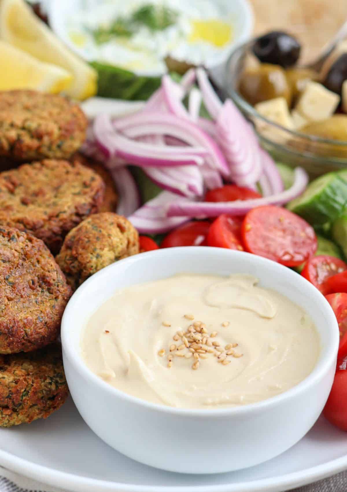 tahini lemon sauce in a white ramekin surrounded by falafel and veggies,